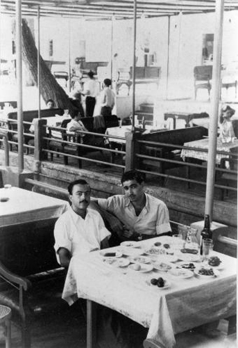 גמליאל כהן ושמעון חורש מתאווררים בזחלה (סוריה), ליד שולחן עמוס בסלטים וקובה ובקבוק עראק זחלווי, בקיץ הלוהט